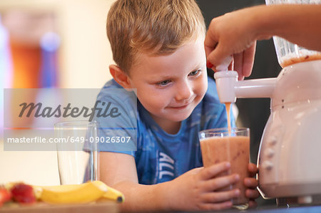 Mother pouring fruit smoothie for son in kitchen