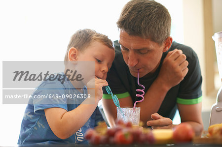 Boy and father sharing fresh smoothie in kitchen