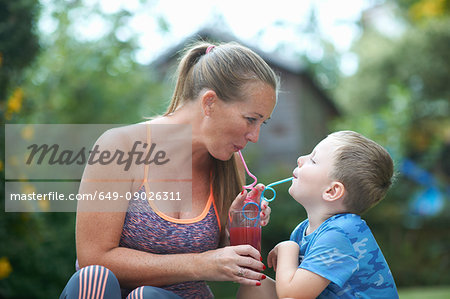 Boy and mother sharing fresh smoothie in garden