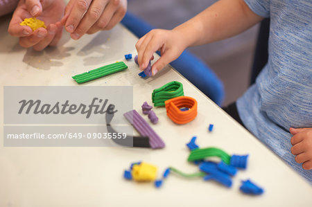 Father and son, sitting at table, playing with modelling clay, close-up