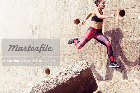 Young female free runner jumping across sea wall Young female free runner jumping across sea wall