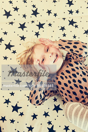 Portrait of female toddler lying on star pattern bed with hands on cheeks