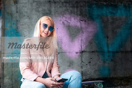 Portrait of young blond female skateboarder wearing sunglasses at skateboard park