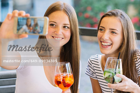 Two young female friends taking smartphone selfie at sidewalk cafe