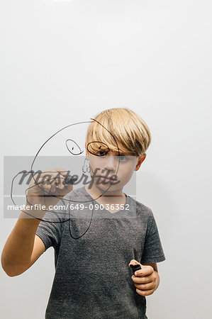 Boy drawing face with marker pen onto glass wall
