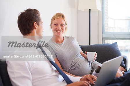 Pregnant couple sitting on sofa typing on laptop