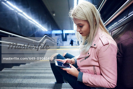 Young woman sitting on underground station stairway looking at smartphone