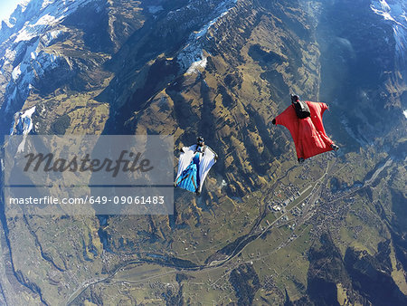 Aerial view of two wingsuit flyers, one on his back facing one in red suit flying above landscape