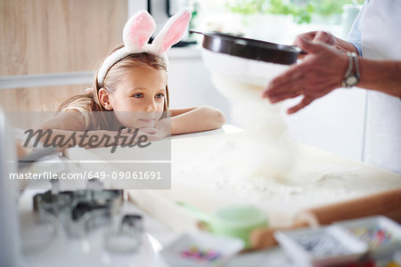 Girl watching grandmother sift flour for easter baking