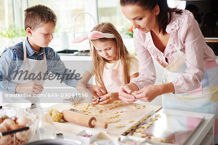 Girl, brother and mother baking easter biscuits at kitchen counter