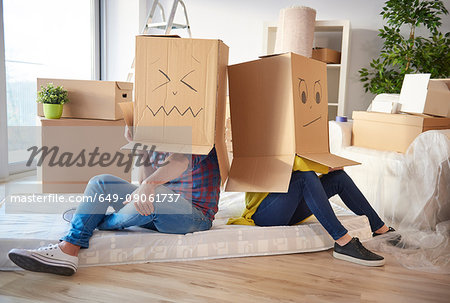 Young couple at home, wearing cardboard boxes on heads, faces drawn on boxes