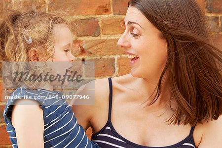 Cute girl and laughing mother by brick wall