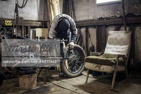 Mechanic adjusting wheel on dismantled vintage motorcycle in workshop