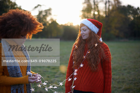 Two young women, in rural setting, young woman wrapped in fairy lights
