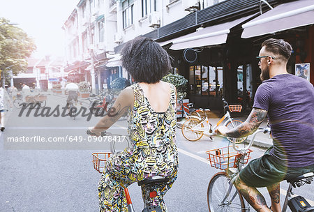 Multi ethnic hipster couple cycling along city street, Shanghai French Concession, Shanghai, China