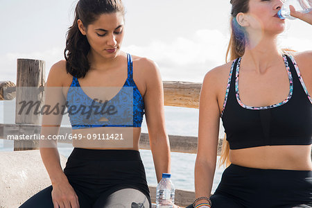 Two young women training together on sea waterfront, drinking bottled water