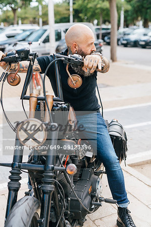 Mature male hipster astride motorcycle, looking over his shoulder