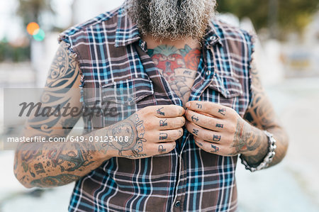 Tattooed male hipster fastening shirt buttons, cropped