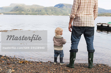 Toddler and father at fjord water's edge looking out, Aure, More og Romsdal, Norway