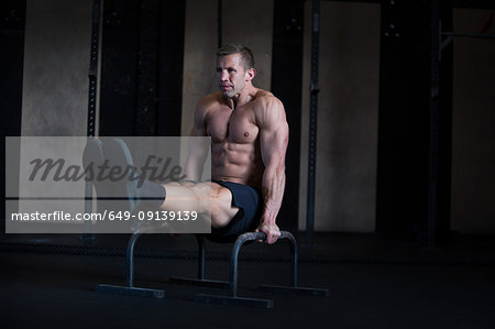 Man exercising in gymnasium, using parallel bars, in L-sit hold