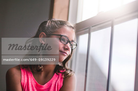 Young girl, wearing glasses, looking out of window