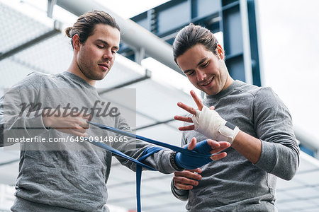Identical male adult twin boxers training outdoors, bandaging hands with hand wraps