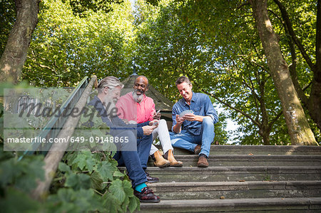 Three mature men, outdoors, sitting on steps, playing cards, low angle view