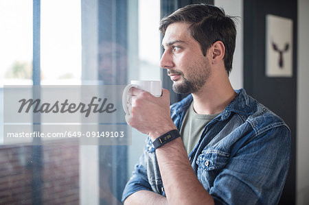 Young man drinking coffee while looking out of  office window