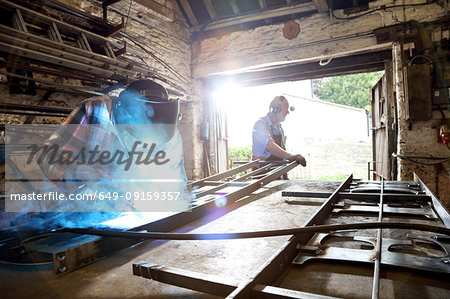 Senior blacksmith and son welding metal on workbench in blacksmiths shop