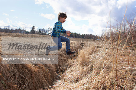 Boy jumping across field ditch