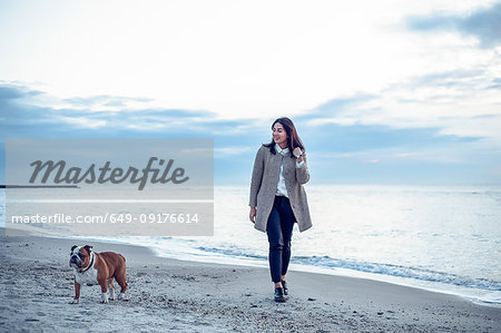 Young woman walking along beach with pet dog