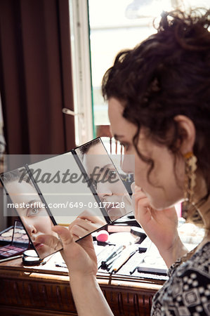 Young woman applying make up in bedroom