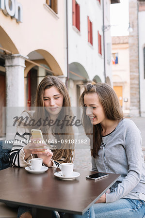 Girlfriends using mobile phone at cafe, Belluno, Veneto, Italy