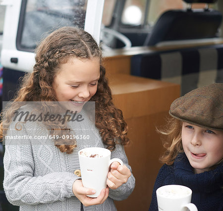 Girls drinking hot chocolate beside camper van