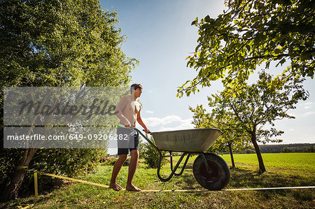 Man pushing wheelbarrow on tight rope Stock Photo Masterfile