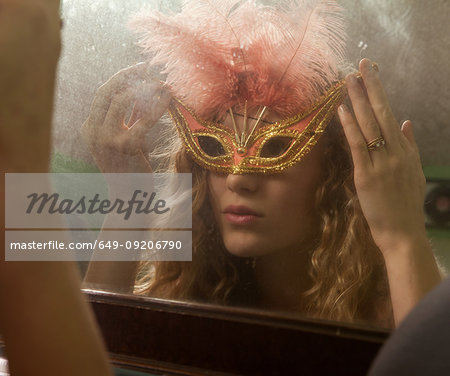 Teenage girl wearing masquerade mask in front of mirror