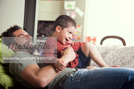 Father reclined on sofa with son on lap