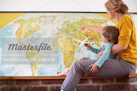 Boy and mature woman sitting in front of world map, playing with aeroplane
