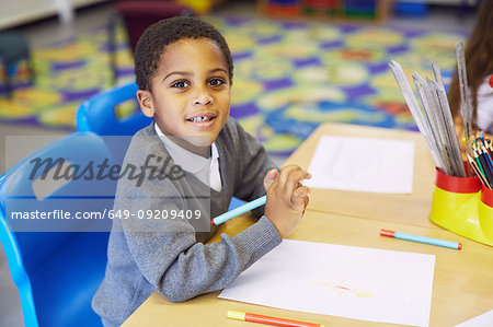 Portrait of boy drawing at desk in elementary school classroom