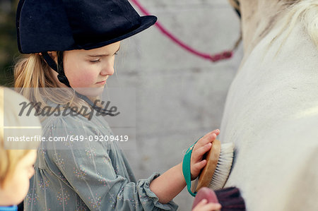 Girl and brother grooming pony at stable