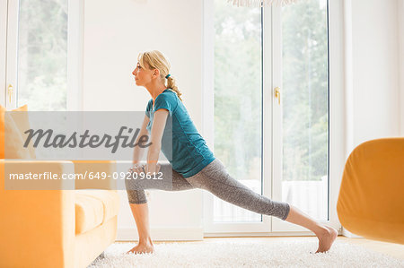 Mature woman doing lunge stretch exercise in living room