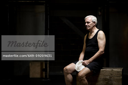 Senior man sitting resting in dark crossfit gym