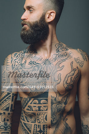 Portrait of  young man with beard, bare chest covered in tattoos