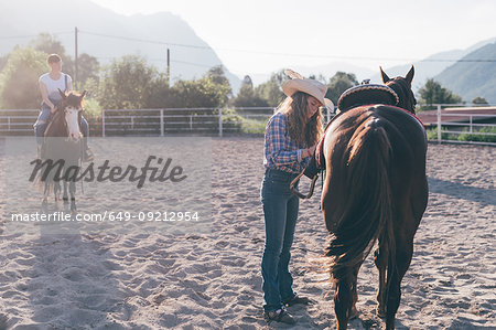 Cowgirl saddling horse in rural equestrian arena, Primaluna, Trentino-Alto Adige, Italy
