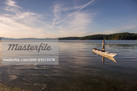 Young female kayaker standing looking out from kayak, Quadra Island, Campbell River, Canada