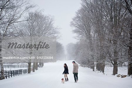 Young couple walking dog in snow covered forest, rear view, Ontario, Canada