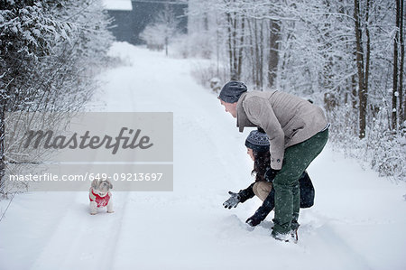 Young couple playing with dog in snow covered forest, Ontario, Canada