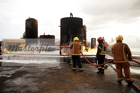 Firemen training, spraying firefighting foam onto oil storage tank fire at training facility