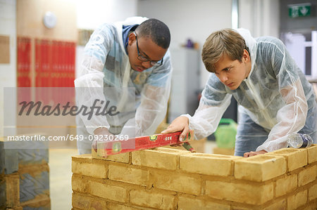 Male higher education students building brick wall in college workshop