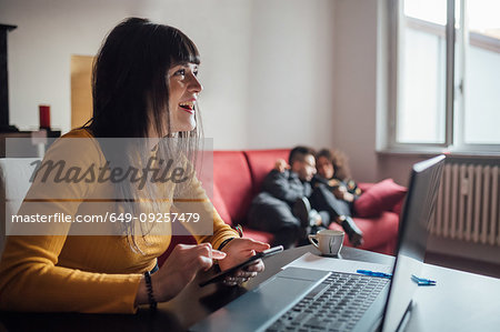 Woman using smartphone, friends relaxing in background in home office